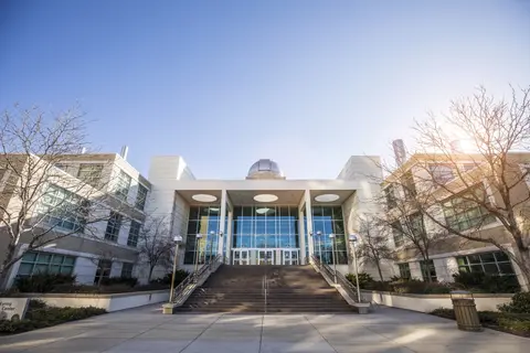 Exterior view of a large modern building with a central staircase and a dome on top.