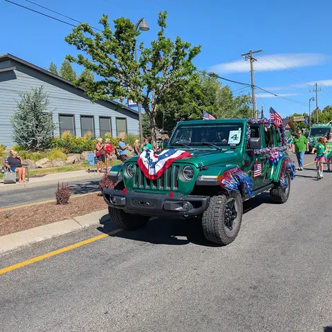 A decorated green jeep drives down a street during a parade.