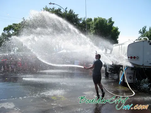 A person sprays water from a hose connected to a water truck in front of a crowd.