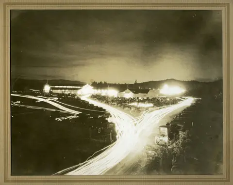 A historic nighttime photograph showing light trails from vehicles and buildings in the background.