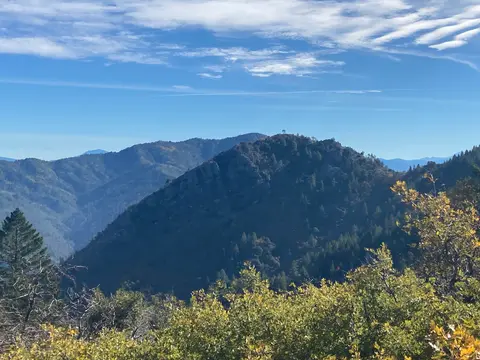 A scenic view of heavily forested mountain ridges under a blue sky with clouds.