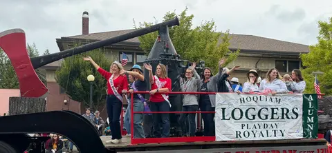 A group of people wave from a parade float featuring a large axe and banner.