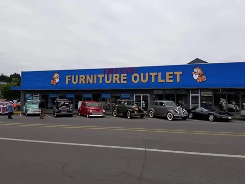An exterior view of a furniture store with several classic cars parked in front.