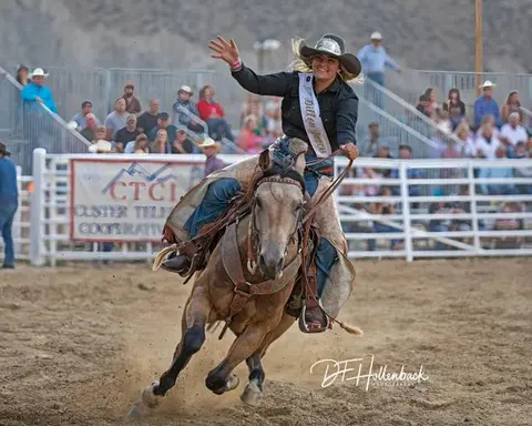 A cowgirl waving while riding a horse at a rodeo arena.