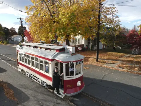 A vintage red and white streetcar drives along tracks on a street with autumn trees.