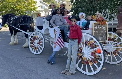 People pose with a horse-drawn carriage adorned with autumn decorations.