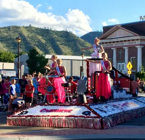A parade float with people in pink dresses moves down a street.
