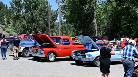 A car show displays classic vintage vehicles outdoors with people walking around them.