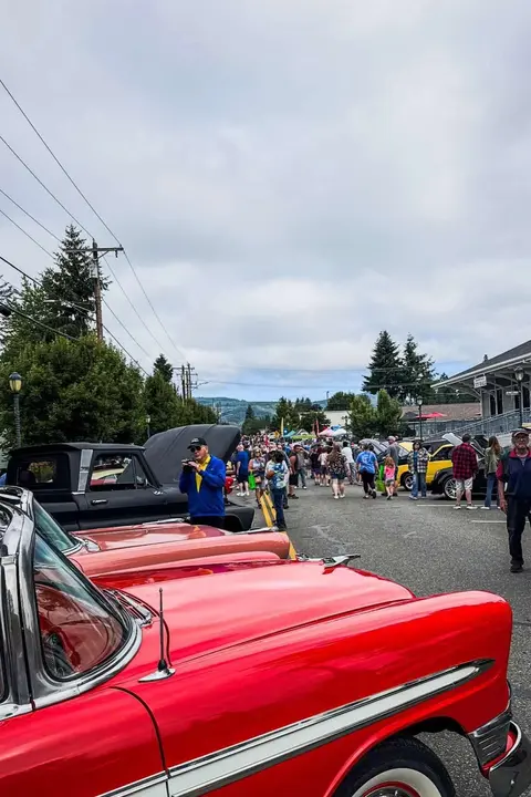 A classic car show fills a street with vintage vehicles and people walking around.