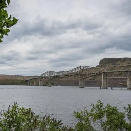 A metal bridge spans across a body of water with hills in the background.
