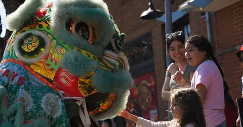 A child reaches out to touch a colorful lion dance costume outdoors.