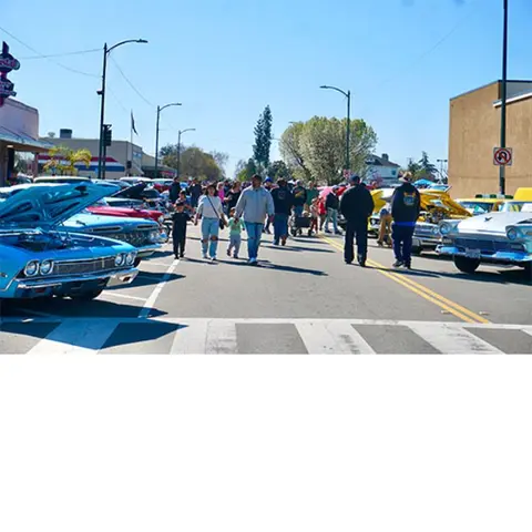 People walking along a street lined with classic cars at a car show.