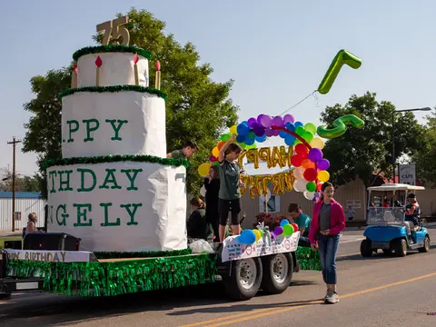 A parade float designed like a large birthday cake with people around it.