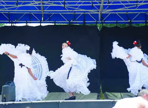 Three dancers perform on a stage wearing white ruffled dresses.