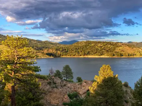 A scenic view of a lake surrounded by forested hills and a cloudy sky.