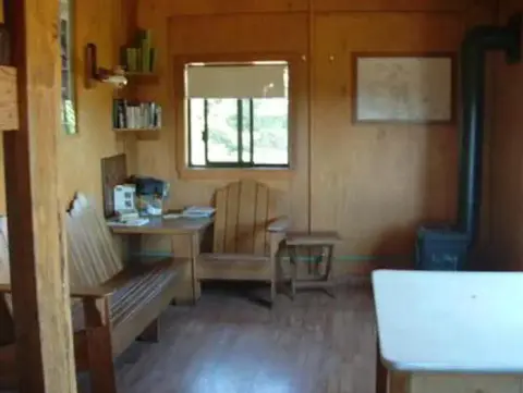 An interior view of a wooden cabin with a bench, table, and stove.