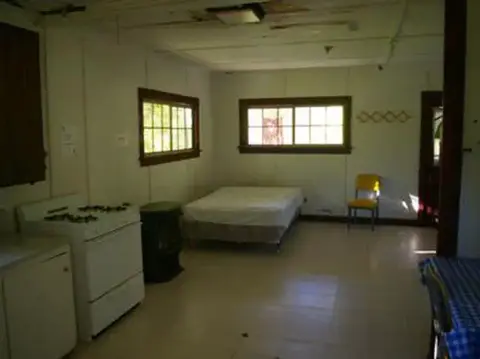 An interior view of a rustic room with a bed, stove, and kitchen area.