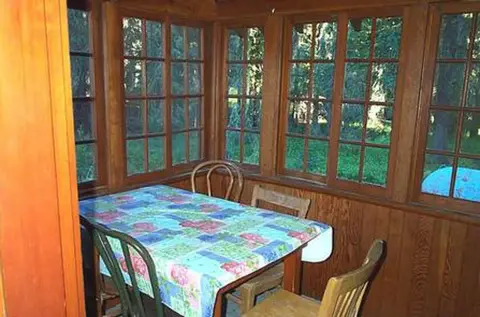A dining table inside a wood-paneled room with many windows overlooking trees.