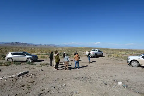 A group of people gather in a desert landscape near parked vehicles.