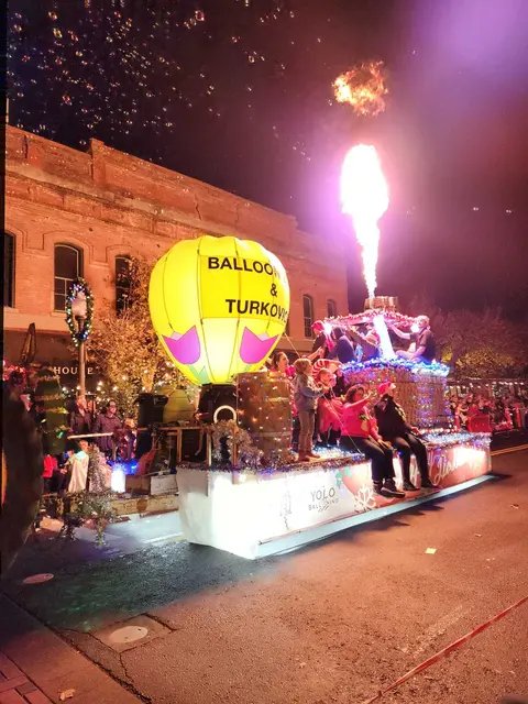 A decorated parade float with a hot air balloon model and burning burner at night.