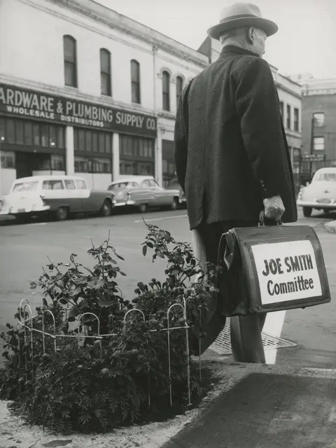 A historic photo shows a man walking down a street carrying a briefcase with a sign.