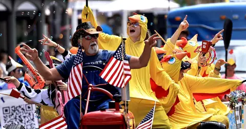 People in costumes participate in a parade, riding a small vehicle decorated with American flags.