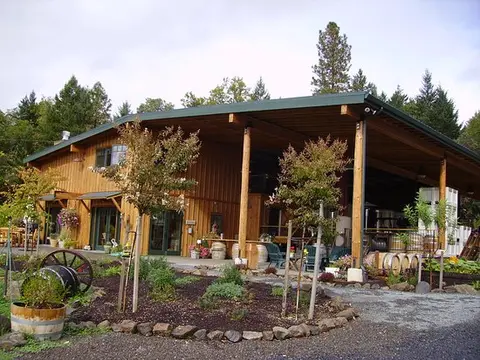Exterior view of a wooden building with a large covered porch and landscaping in front.