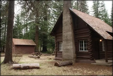 A rustic log cabin sits among tall trees in a forest.