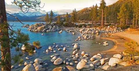 A scenic view of a rocky lake shore with mountains in the background.