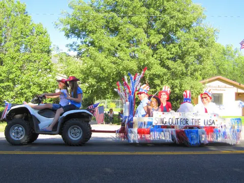 People ride an ATV pulling a parade float decorated with patriotic themes.