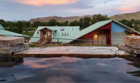 A view of buildings and mountains from a hot spring pool at dusk.