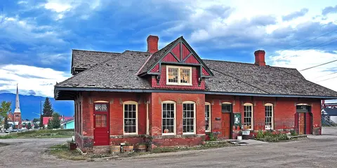 A red brick building with a shingled roof stands beside a dirt area.