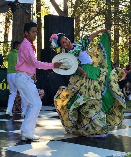 Dancers in traditional costumes perform on an outdoor checkered stage.
