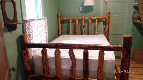 A rustic log-frame bed in a green-walled bedroom.