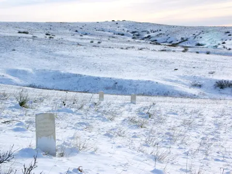 A snowy hillside landscape with several grave markers scattered across the snow.