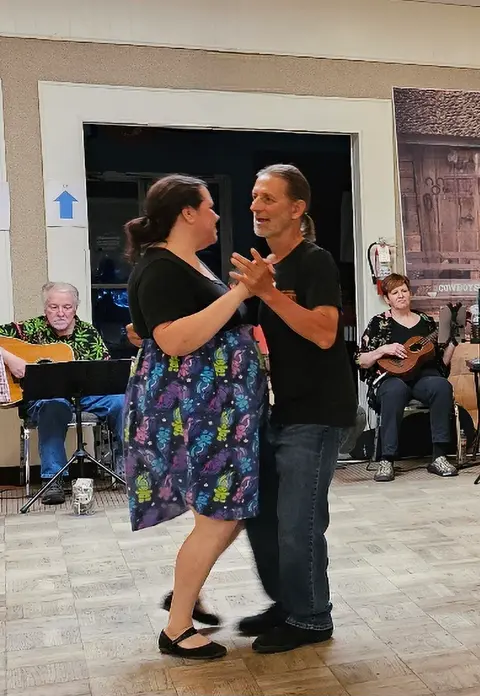 A couple dances indoors while musicians play instruments in the background.
