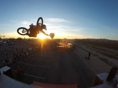 A BMX rider performs a trick in mid-air above a crowd during sunset.