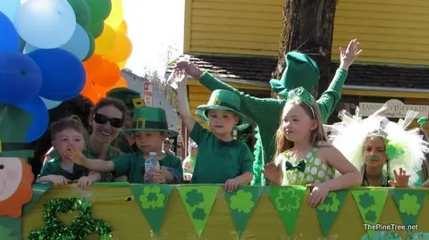 People dressed in green celebrate on a float decorated with balloons and shamrocks.