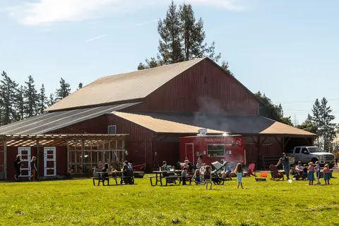 People gathering outside a large red barn on a sunny day.