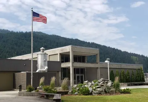 A modern building with an American flag in front and mountains in the background.
