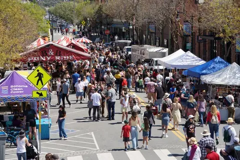 A busy street fair fills a city street with tents and crowds of people.