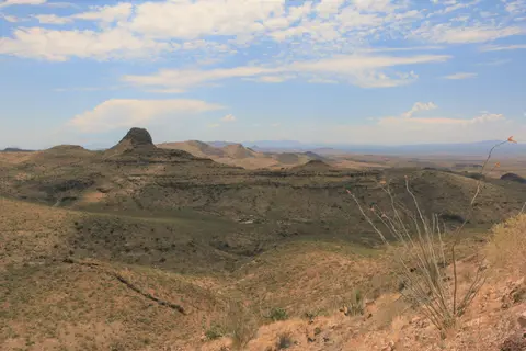 A scenic view of a dry, mountainous desert landscape under a cloudy blue sky.