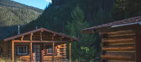 Log cabins set against a mountain and forest backdrop.