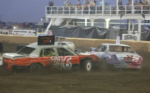 Two demolition derby cars crashing into each other on a dirt track.