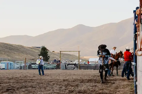 People at a rodeo arena with mountains in the background.