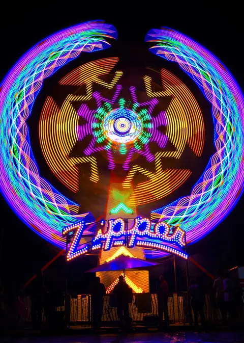 A long exposure photo shows a brightly lit carnival ride spinning at night.