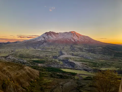 A large volcano with snow-capped peaks under a sunset sky.