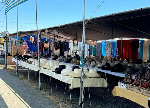 A vendor's stall at an outdoor market displays many cowboy hats on tables under awnings.