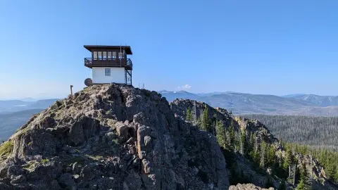 A fire lookout tower sits atop a rocky mountain peak.
