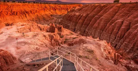 A metal staircase descends into a canyon with dramatic red rock formations.
